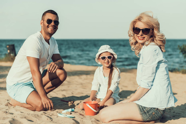 Padre y esposa e hija están sentados en la playa, divirtiéndose
. - Foto, imagen