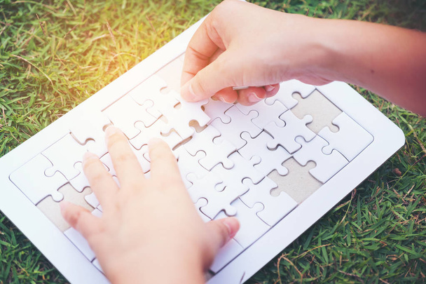 hands connecting puzzle pieces on green grass background - Photo, Image