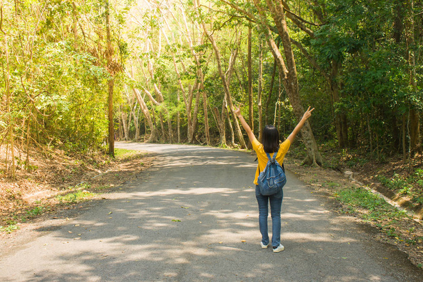 Donna sola viaggiatore o zaino in spalla a piedi lungo la strada contryside tra alberi verdi, alza le mani sopra la testa e sensazione di felicità
. - Foto, immagini