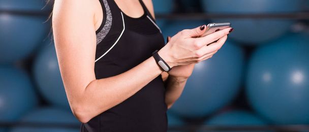 Close up of woman using cell phone and fitness tracker in gym - Valokuva, kuva