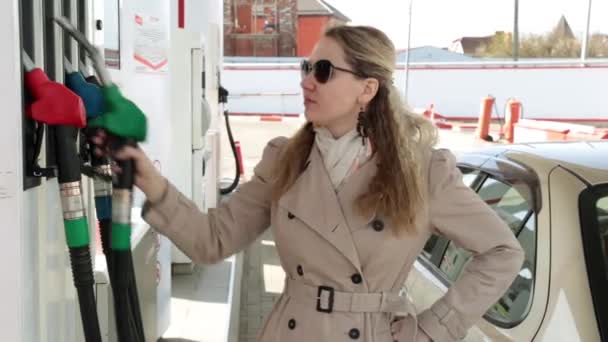Eine Frau an einer Tankstelle hält sich eine Benzinpistole an den Kopf. Teure Kraftstoffe, Benzin. - Filmmaterial, Video