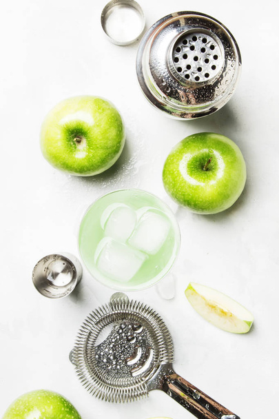 Alcoholic cocktail with green apple and dry vermouth, syrup, lemon juice and ice cubes. Bar tools, gray stone background, top view - Photo, Image