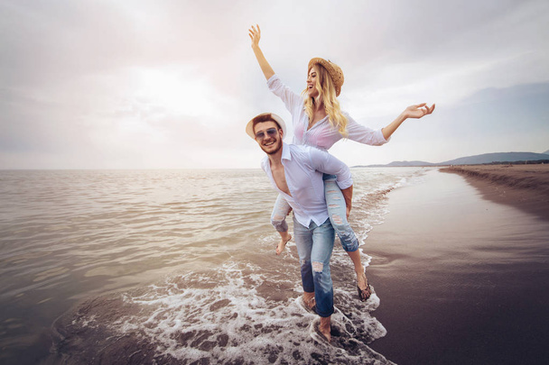 Щаслива пара закохалася у пляжні літні канікули. Радісна дівчина, що стрибає на молодого хлопця, розважається
. - Фото, зображення