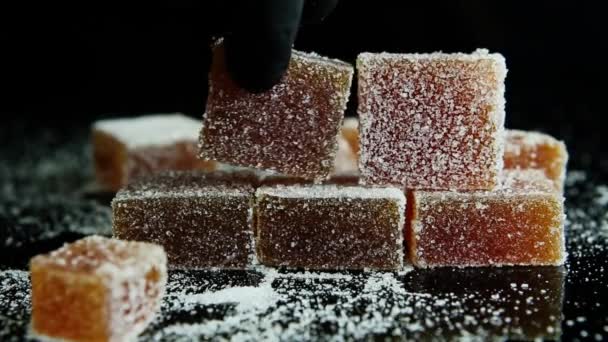 suikerwerk hand bouwt een piramide van sinaasappel marmelade bedekt met suiker op zwarte spiegel achtergrond - Video