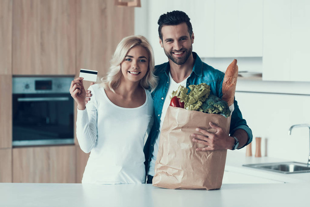 Ενηλίκων ευτυχισμένο ζευγάρι στέκεται στην κουζίνα με το πακέτο των προϊόντων. - Φωτογραφία, εικόνα