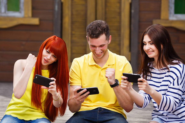 Group of three friends play mobile video game outdoors, winners  - Photo, Image