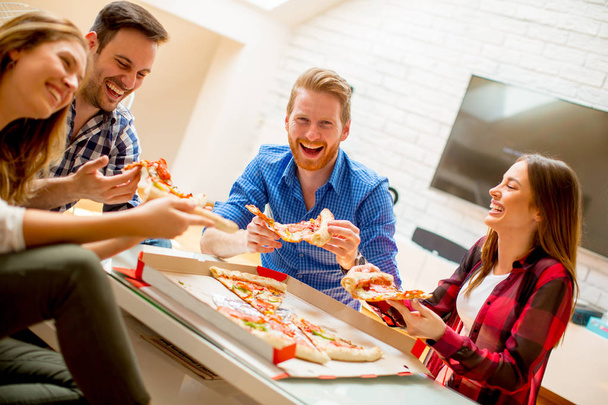 Grupo de jóvenes amigos comiendo pizza en casa y divirtiéndose
 - Foto, Imagen