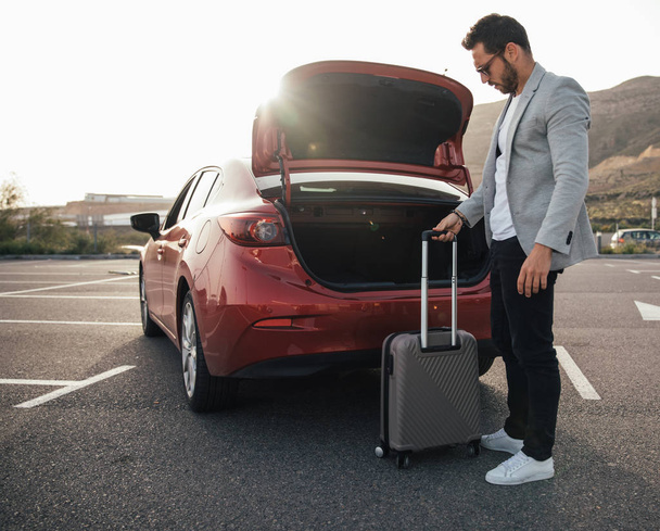 Man traveler putting suitcase in car trunk - Фото, изображение