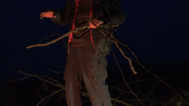Volwassen man breekt en knipt droge branche van boom voor vreugdevuur in bergen bij nacht - Video