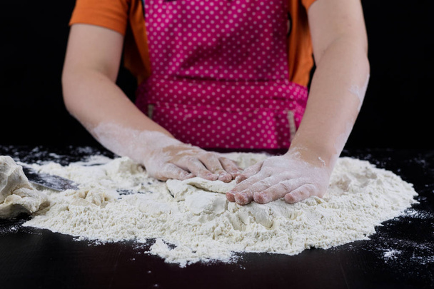 Kneading dough on a black table in a bakery. Baker's hands prepa - Фото, изображение