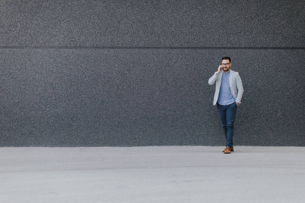Молодий чоловік ходить і розмовляє по мобільному телефону надворі
 - Фото, зображення