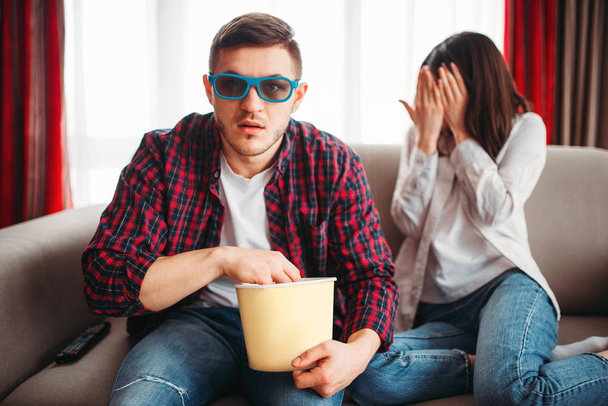 Pár ül a kanapén, férfi 3D-s szemüveg a kezét néz film pattogatott kukorica, rémült nő bezárja az arcát a kezével - Fotó, kép