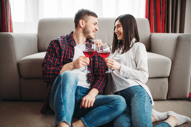 влюбленная пара сидит на полу напротив дивана, пьет красное вино, романтический вечер
 - Фото, изображение