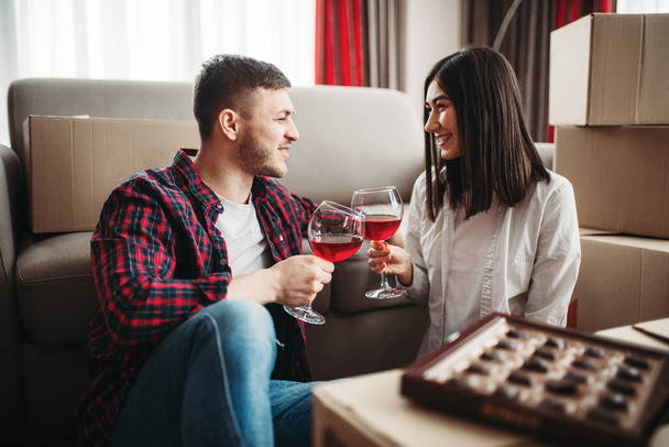 miłość para siedzi na podłodze w pobliżu kartony, picie czerwonego wina i doceniają, Przeprowadzka do nowego domu - Zdjęcie, obraz
