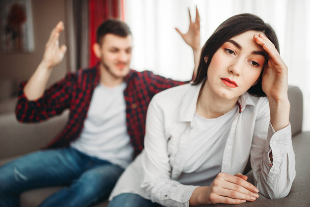 stressaantunut vaimo istuu sohvalla, vihainen aviomies huutaa taustalla, perheen konflikti. Onneton mies ja nainen riidoissa
 - Valokuva, kuva