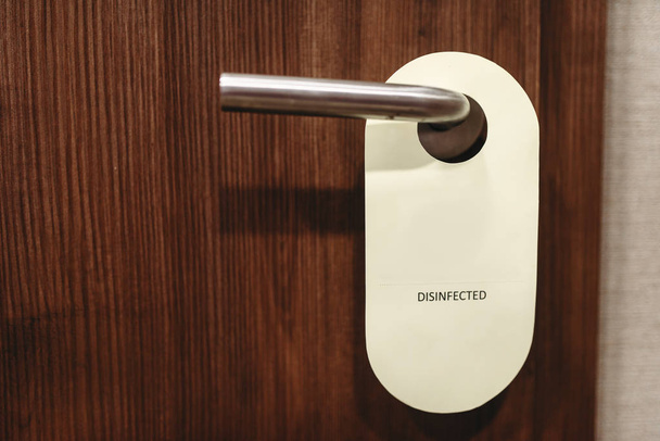 Señal de la puerta advirtiendo sobre la desinfección. Desinfectado, letrero informativo en la manija de la puerta de madera
 - Foto, Imagen