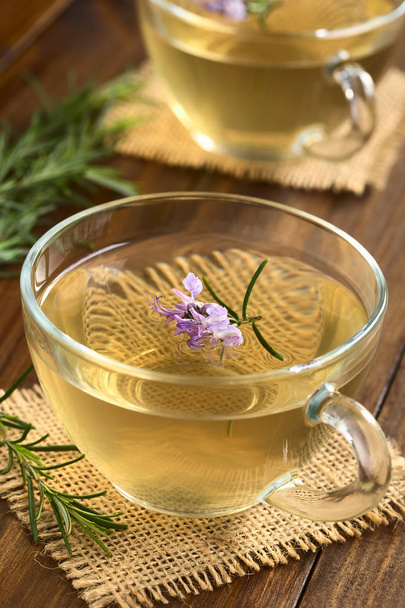 Frissen készített rozmaring gyógynövény tea üveg csésze, rozmaring virágok, természetes fény (szelektív összpontosít, a hangsúly az első virágok a sötét fa fényképezett körítve) - Fotó, kép