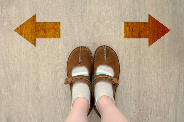 Pohled shora hnědé boty s různými hnědé rozhodnutí šipkou. Dvojice nohou stojící. Boty chůze směrem na pozadí dřevěná podlaha - Fotografie, Obrázek