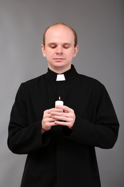 Portrait of young Pastor holding candle in his hand,on gray background - Photo, image