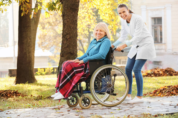 Disabled senior woman and young nurse in park - Foto, afbeelding