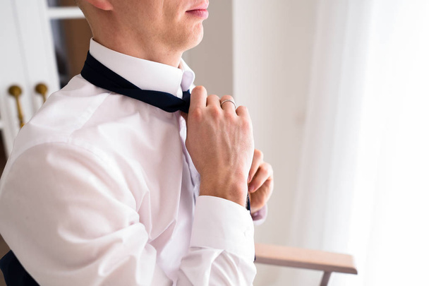 A man in a white shirt ties a tie - Foto, imagen