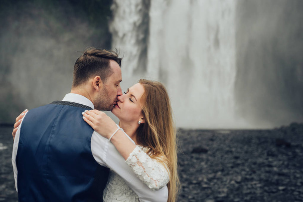 Happy married couple kissing near waterfall at daytime - Zdjęcie, obraz