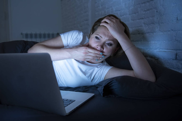 young beautiful, caucasian, red haired, internet addicted woman working and surfing on her laptop in bed at home late at night in dark room. Yawning exhausted. looking bored sleepless and tired. - 写真・画像