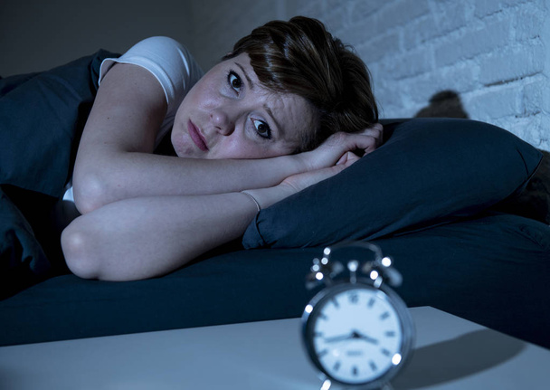 Young attractive red haired caucasian woman lying in bed late at night trying to sleep suffering from insomnia, nightmares or sleeping disorders. looking stressed and exhausted. - Photo, Image