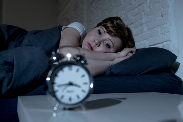 Young attractive red haired caucasian woman lying in bed late at night trying to sleep suffering from insomnia, nightmares or sleeping disorders. looking stressed and exhausted. - Photo, image