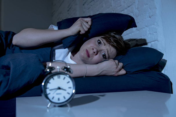 Молодая привлекательная рыжеволосая кавказская женщина, лежащая в постели поздно ночью, пытается уснуть, страдая бессонницей, кошмарами или расстройствами сна. выглядящие напряженными и изможденными
. - Фото, изображение