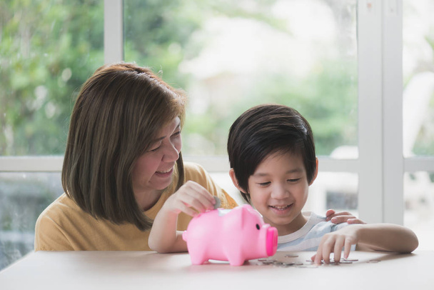 Cute Asian child putting a coin into a piggy bank - Photo, Image