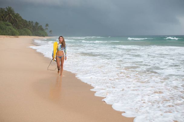 Female surfer walking along the ocean with a board in hands. - Fotoğraf, Görsel