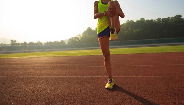 Jeune femme étirant les jambes avant de courir pendant la matinée ensoleillée sur le stade
  - Photo, image