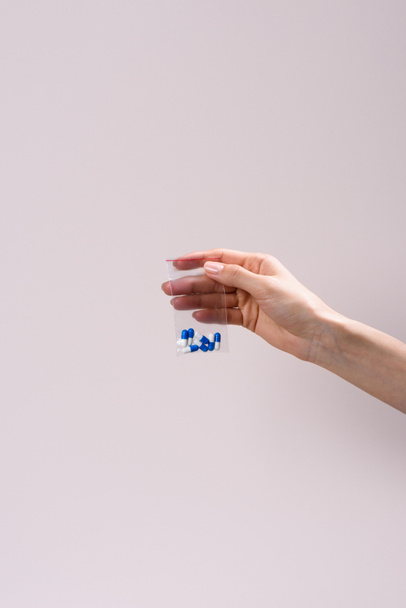 bijgesneden schot van vrouw met zakje met ritssluiting met pillen geïsoleerd op grijs - Foto, afbeelding