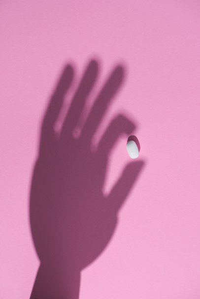 Widok z góry cień ręki trzymającej pigułka na powierzchni różowy - Zdjęcie, obraz