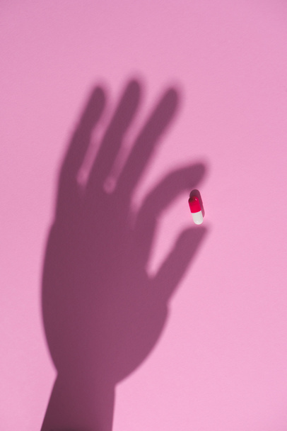 felülnézet kezében kábítószer kapszula rózsaszín felületen árnyékában - Fotó, kép