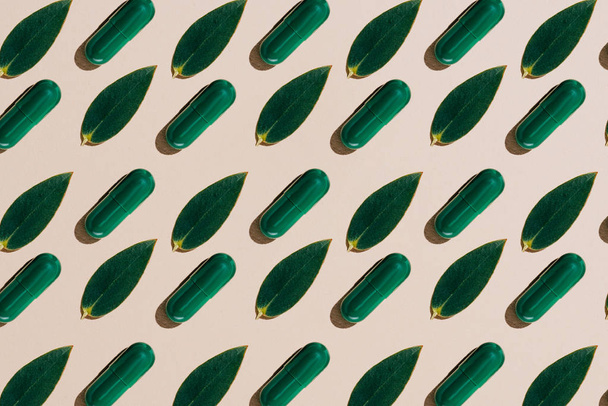 vista superior de las cápsulas de fitoterapia con hojas verdes en filas patrón sobre la mesa beige
 - Foto, Imagen
