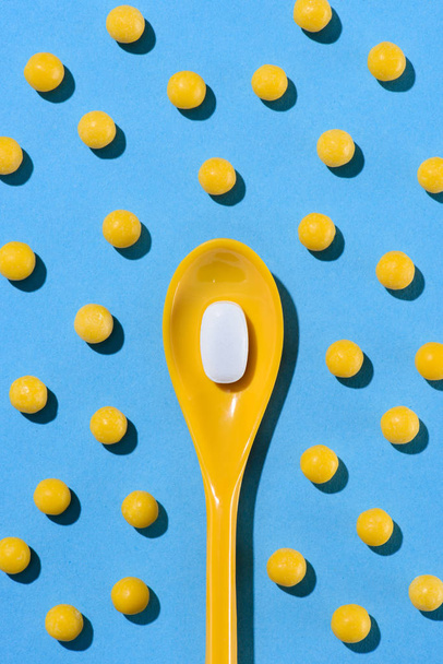 top view of yellow plastic spoon with white pill surrounded with pills on blue - Fotoğraf, Görsel
