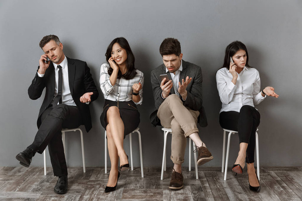 Διαφυλετικό επιχειρηματίες στην επίσημη ένδυση με smartphones περιμένει δουλειά συνέντευξη  - Φωτογραφία, εικόνα