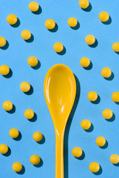 vista superior de la cuchara de plástico amarillo rodeado de píldoras en azul
 - Foto, Imagen