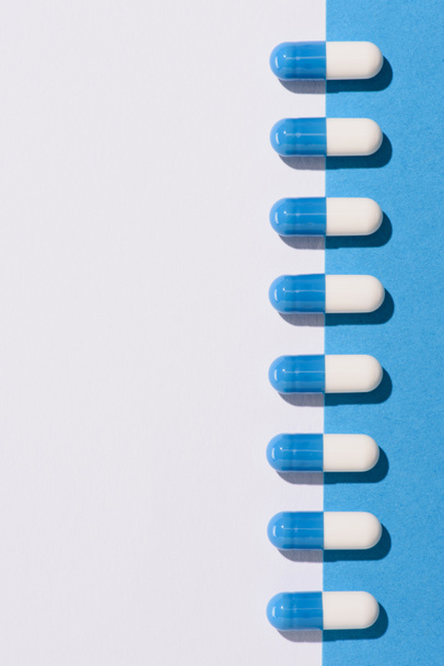 vista superior de la fila de cápsulas de medicamentos en la mitad de la superficie blanca y azul
 - Foto, Imagen