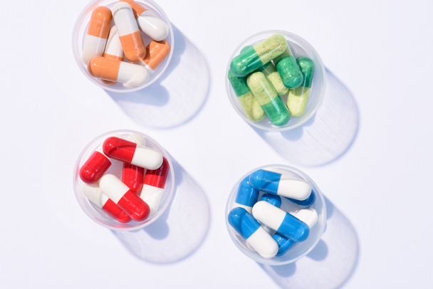 вид сверху различных красочных таблеток в пластиковых банках на белом
 - Фото, изображение