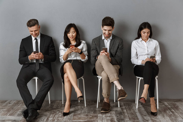 χαμογελώντας διαφυλετικός επιχειρηματίες χρησιμοποιούν smartphones, ενώ περιμένουν για συνέντευξη για δουλειά - Φωτογραφία, εικόνα