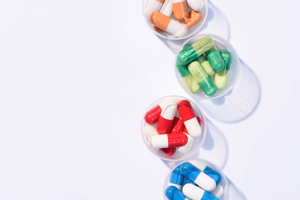 bovenaanzicht van verschillende kleurrijke pillen in kunststof kommen op wit - Foto, afbeelding