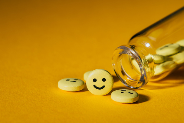 Nahaufnahme von Pillen mit Smiley-Gesichtern und Glasflasche auf gelb - Foto, Bild