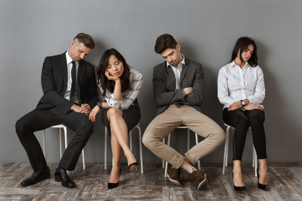 cansado interracial negocios personas en formal desgaste durmiendo en sillas mientras espera para trabajo entrevista
 - Foto, Imagen
