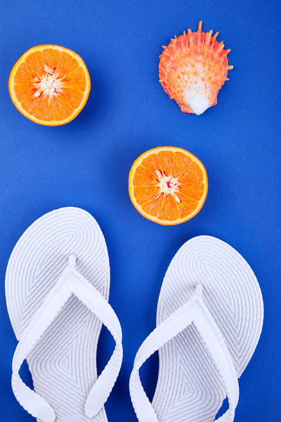 Conceito de verão. Chinelos brancos, fruta laranja, concha sobre fundo de papel azul. Deitado. Espaço de cópia
 - Foto, Imagem