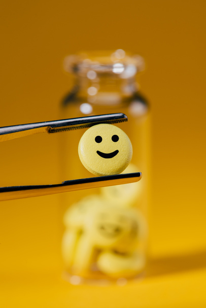 primer plano de la píldora con la cara sonriente en pinzas y botella de vidrio en amarillo
 - Foto, Imagen