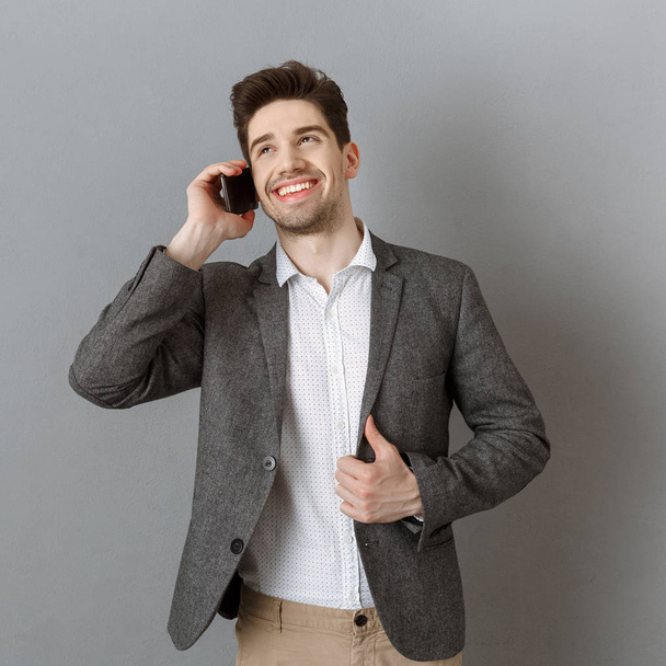 portrait of smiling businessman talking on smartphone against grey wall background - Fotografie, Obrázek