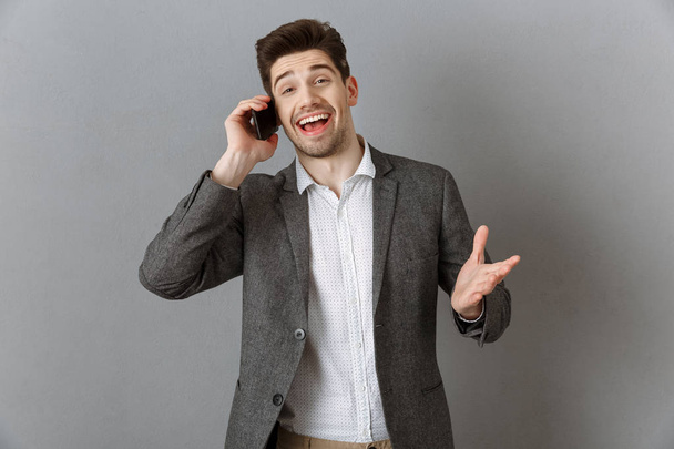 портрет емоційного бізнесмена, який говорить на смартфоні на сірому фоні стіни
 - Фото, зображення